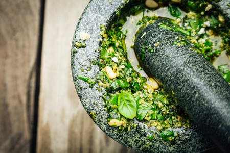 Preparing savory Italian pesto sauce with fresh ingredients crushing a mixture of garlic, pine nuts,olive oil, fresh basil and parmesan cheese in a rustic stone pestle and mortar, close up high angleの写真素材