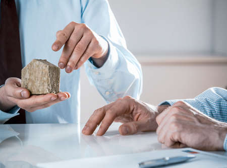 Close Up of Businessman Holding Small Rustic House Model in Meeting with Co-Workers in Real Estate Concept Imageの写真素材