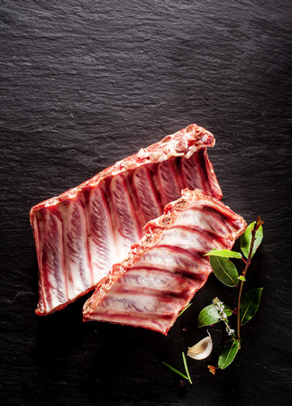 High Angle View of Raw Split Boar Spare Ribs with Fresh Herbs on Textured Grey Surface with Copy Spaceの写真素材
