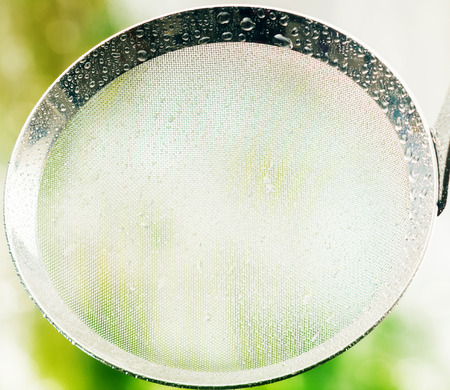 High Angle Close Up of Clean Metal Strainer Covered with Rain Water Drops Outdoors with Fresh Green Vegetation Backgroundの写真素材