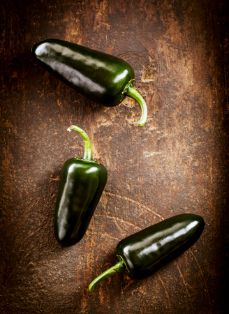 Three fresh whole jalapeno lying on an old rustic wooden table with copyspace, overhead viewの写真素材