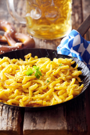 Traditional Bavarian spaetzle, or boiled egg noodles, served with beer and a salty pretzel on a rustic wooden table for a tavern lunchの写真素材