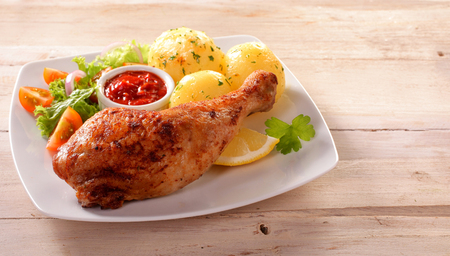 Close Up of Healthy Chicken Dinner - Roasted Chicken Leg on White Plate with Fresh Green Salad and Roasted Potatoes Served on Rustic White Wooden Table Surface with Copy Spaceの写真素材