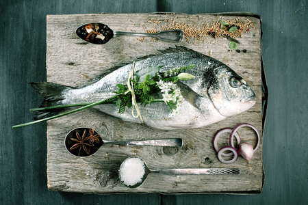 High Angle View of Fresh Whole Raw Fish on Rustic Wooden Cutting Board Surrounded by Fresh Herbs and Spices for Seasoningの写真素材