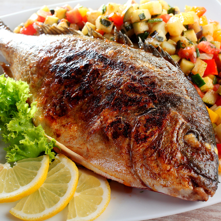 Close Up of Roasted or Grilled Whole Fish Garnished with Lettuce and Lemon Wedges Served on Bed of...