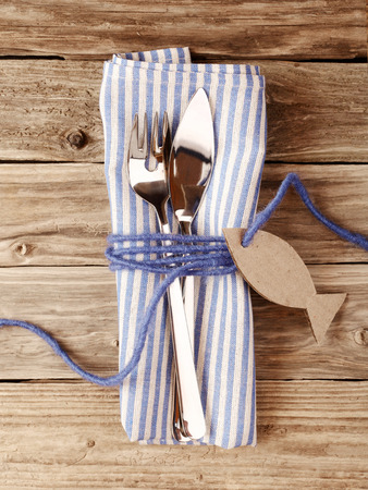 Close up Fork and Knife for fish Tied on Striped Purple Napkin with Fish Shaped Tag on Top of a Wooden Tableの写真素材