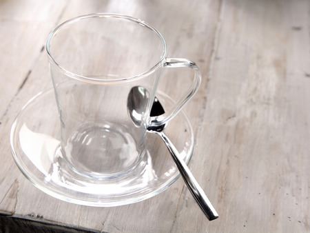 Empty clear glass mug or cup and saucer standing ready with a teaspoon on an old weathered wood table for making a cup of hot refreshing teaの写真素材