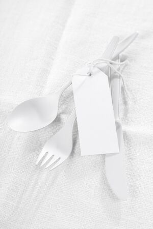 Pure white - a monochromatic all white concept for food or catering with white utensils tied with a blank white gift tag over a textured white tablecloth with copyspaceの写真素材