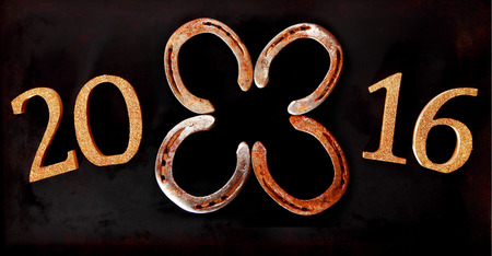 2016 New Year horizontal banner background with four lucky horseshoes arranged as a four-leaf clover or shamrock in the center of the date symbolising Good Luck Wishes over a dark backgroundの写真素材