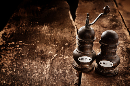 Old-fashioned labelled salt and pepper mills standing side by side on a rustic wooden table with copyspace for food placement, high angle viewの写真素材