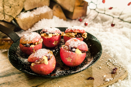 Christmas baked stuffed fresh red apples with a star decoration and raisin and walnut stuffing sprinkled with sugar on a pan outdoors on a rustic wooden board in winter snowの写真素材