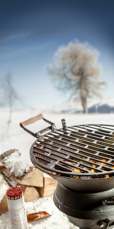 Empty BBQ grill with hot coals standing outdoors in a snowy winter landscape with condiments and spices ready for a winter barbecue partyの写真素材