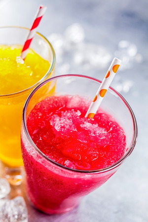 High Angle Still Life View of Refreshing and Colorful Frozen Fruit Slush Granita Drinks - Yellow and Red - in Glasses with Patterned Straws on Cold Metal Surface with Copy Spaceの写真素材