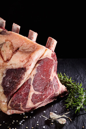Close up on piece of uncooked cote de boeuf beef ribs with garlic and rosemary over black backgroundの写真素材