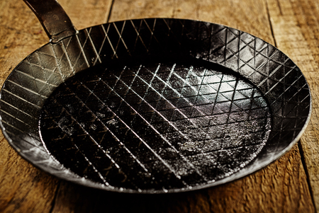 Close up on empty single black cast iron pan with scoring lines inside over dark thick brown wooden tableの写真素材