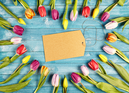 Heart shaped romantic frame of fresh spring tulips arranged with radiating stems and the flowers forming the heart over a blue wooden background with central blank gift tag for your greetingの写真素材
