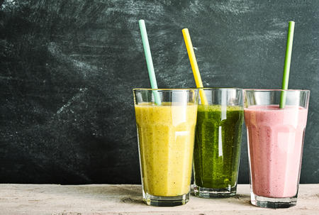 Trio of healthy fruit and vegetable smoothies - berry, kale and banana and almond - with straws on a rustic wooden table with slate background with copy spaceの写真素材