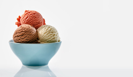One scoop each of strawberry vanilla and chocolate flavored ice cream in a blue bowl on a white...