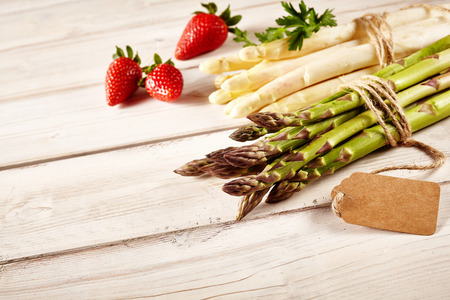 Three strawberries beside two bundles of raw green and white asparagus tied with string and blank price tagの写真素材