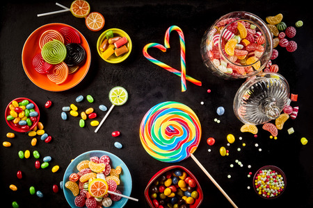 Candy canes placed to form heart besides large sucker, jelly beans and bowls of other tasty confections against a black backgroundの素材 [FY31057783252]