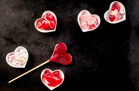 Sweet confections sitting in ceramic bowls besides heart shaped lollipop against a black backgroundの写真素材