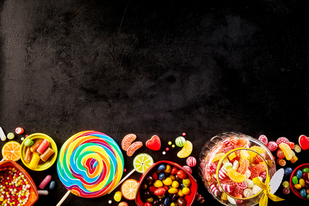 Black background with row of confections at bottom featuring large spiral colored sucker and glass jar filled with hard confectionsの写真素材