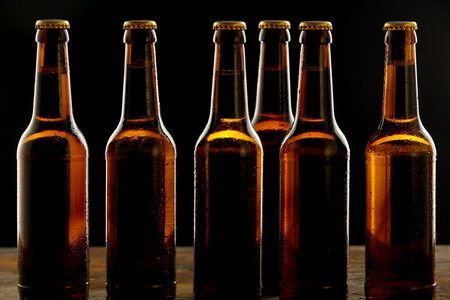 Row of ice cold unlabelled unopened brown beer bottles standing on a pub or tavern counter on a shadowy background in a branding and advertising concept for Oktoberfestの写真素材