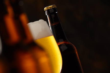 Glass of glowing golden frothy beer in a selective focus view between to beer bottles with copy...