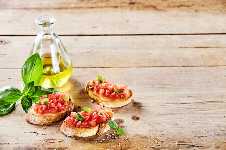 Tasty Italian tomato bruschetta with olive oil on toasted slices of baguette served with fresh basil on a rustic wooden table with copy spaceの写真素材