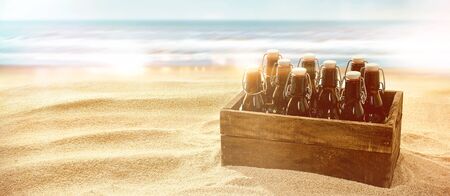Crate of beers in brown glass bottles with cork on a sunny tropical beach close to the ocean on a hot summer day with copy spaceの写真素材