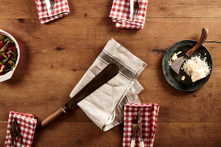 Top down view on four settings of napkins and utensils beside dish of Parmesan cheese on wooden tableの写真素材