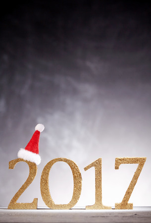 Single little red and white Santa hat perched on golden new year in 2017 decoration over dark to...