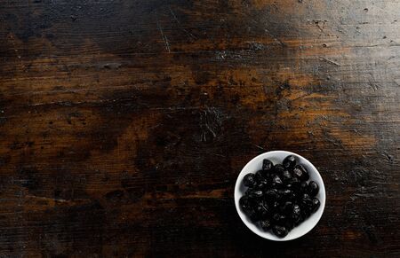 Bowl of cured black olives placed in the corner on a on rustic old dark stained wood background with plenty of copy spaceの写真素材