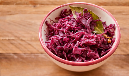 Dish of shredded boiled purple cabbage seasoned with a bay leaf for flavoring viewed close up high angle on wood with copy spaceの写真素材