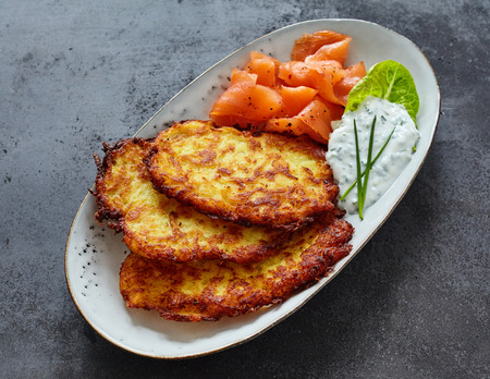 High Angle Close Up of Crisp Fried Potato Rosti Patties on Decorative Plate with Smoked Salmon and Creamy Dill Sauce on Textured Gray Counterの写真素材