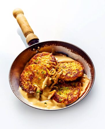 High Angle Still Life of Crisp Golden Fried Potato Pancakes in Cream Sauce with Sliced Apples in Pan with Wooden Handle in front of White Backgroundの写真素材