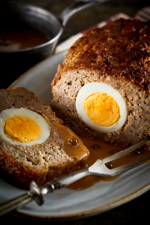Meatloaf with egg inside served with gravy with roast fork, close-up imageの写真素材