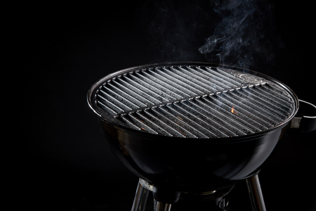 Hot barbecue fire with wisps of smoke from the coals ready for grilling the food in a portable BBQ over a dark backgroundの写真素材