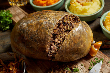 Close up on a sliced open cooked Scottish haggis on a cutting board with side dishes of potato, turnips and carrot, or neeps and tattiesの写真素材