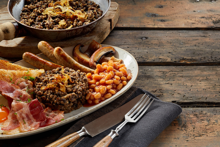 Scottish country breakfast with haggis served with fried egg, beans, mushroom, toast, bacon and sausages on a rustic table with copy spaceの写真素材