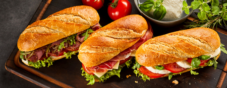 Trio of three fresh long sandwiches made with various types of meat on large serving trayの写真素材