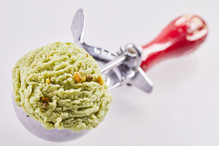Metal scoop full of green artisanal Italian pistachio nut ice cream or gelato with focus to the texture of the dessert and shallow dof over white with copy spaceの写真素材