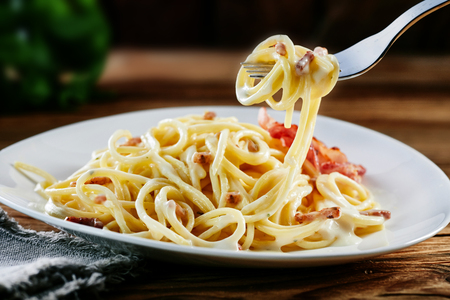 Tasty Italian carbonara spaghetti twirled on a fork ready for eating a mouthful suspended above a plateful of noodlesの写真素材