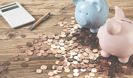 Two piggy banks with calculator and pen on wooden table among saved coinsの写真素材