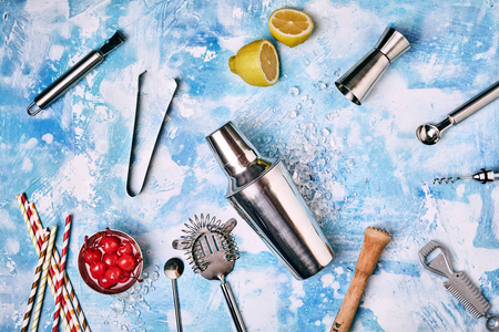 Collection of Cocktail Bar utensils scattered on blue background with lemon and bowl of cherriesの写真素材