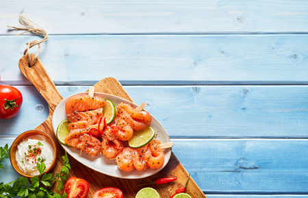 Plate of fresh smoked salmon skewers served with lemon and a Greek tzatziki dip on a wooden board over a rustic blue table with copy spaceの写真素材