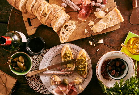 High angle view of bread with wine, pesto, ham and other sides on tableの写真素材
