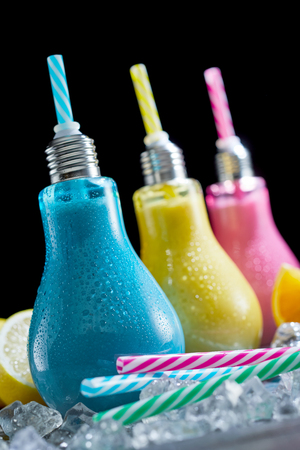 Fun chilled cocktails served in colored light bulb shaped glass containers with straws on a bed of crushed ice in a close up tilted viewの写真素材