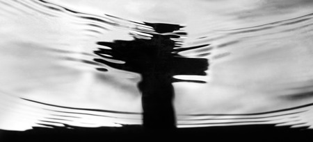 Panoramic banner of a cross gravestone reflected in rippling water for concepts about bereavement, loss, death and mourningの写真素材