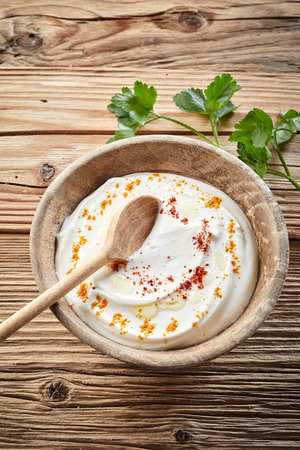 Bowl of seasoned refreshing Indian raita made with natural Greek yogurt and topped with spices in a rustic wooden bowl on wood background in a view from aboveの写真素材